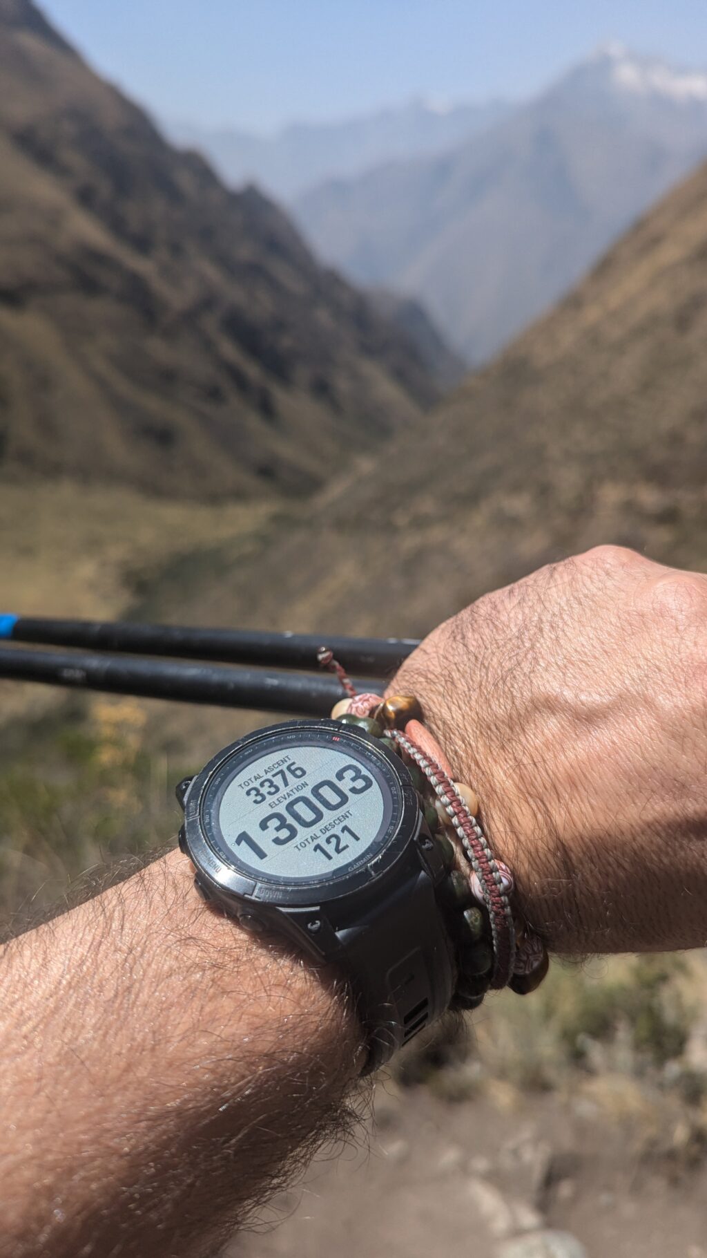 Close-up of a hiker's watch displaying altitude and steps on the Inca Trail, with mountain scenery in the blurred background.