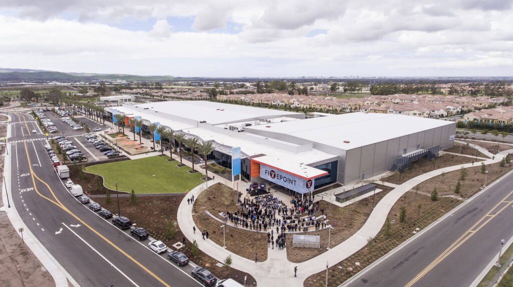 Aerial view of FivePoint Arena in Irvine, showing modern facility design, palm-lined entrance, event plaza, and surrounding residential community