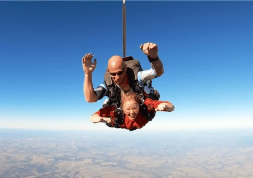 Kristy Durso tandem skydiving with an instructor, freefalling high above a rural landscape under a clear blue sky.