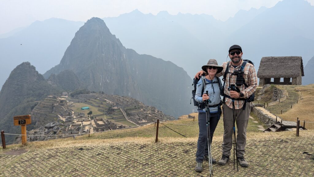 Two hikers standing in front of the iconic Machu Picchu with clear views of the ancient ruins and surrounding mountains in the background.