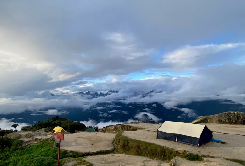 A campsite on the Inca Trail with tents set against a backdrop of clouds and mountain peaks, representing sustainable tourism practices.