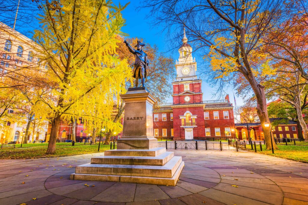 Independence Hall in Philadelphia during autumn, with golden fall foliage and the Barry statue, showcasing the city's historic sensory-inclusive destination