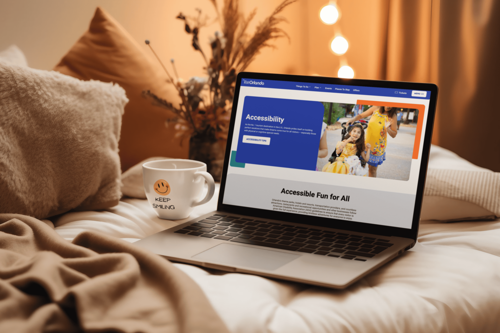Laptop displaying Visit Orlando's accessibility webpage with 'Accessible Fun for All' heading, next to a coffee cup with smiley face in a cozy setting